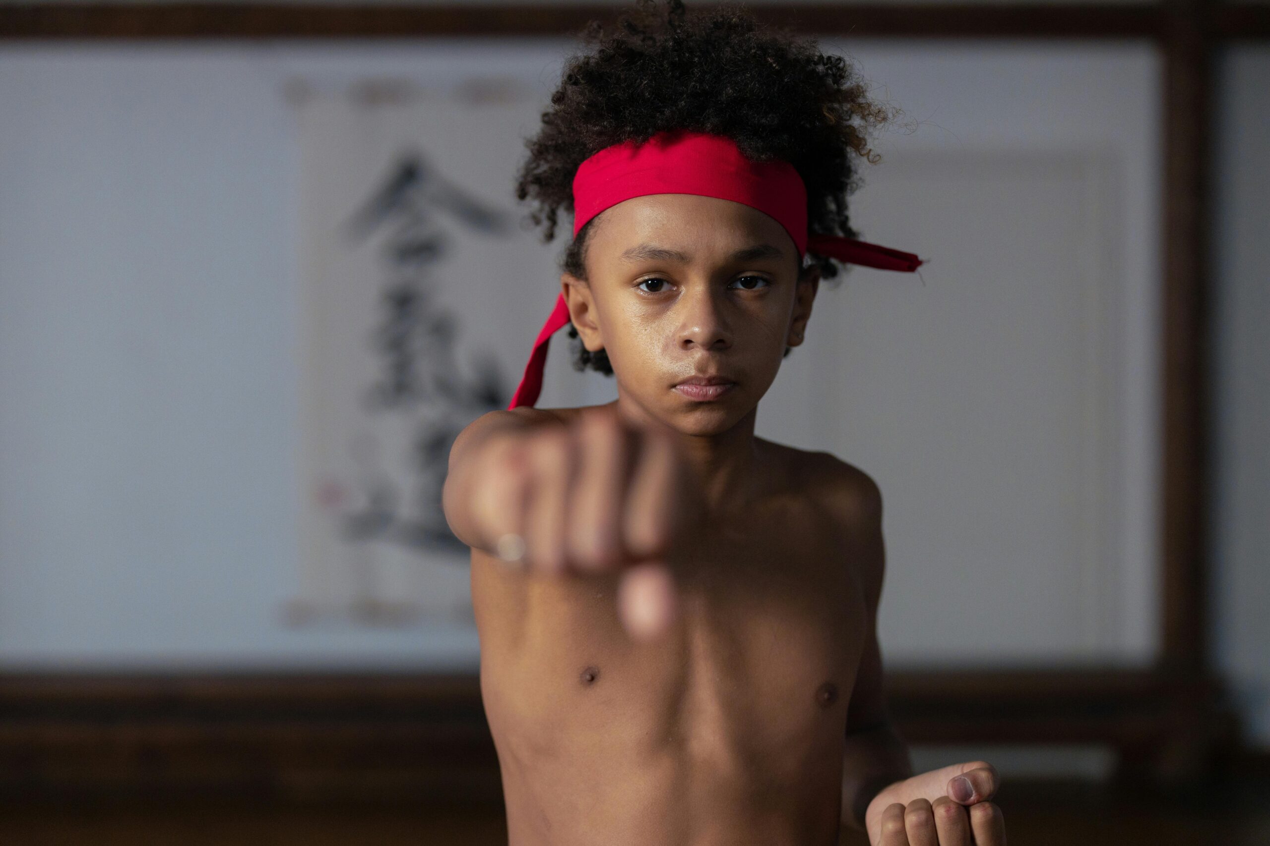 Determined young martial artist practicing a punch in a dojo wearing a red headband.